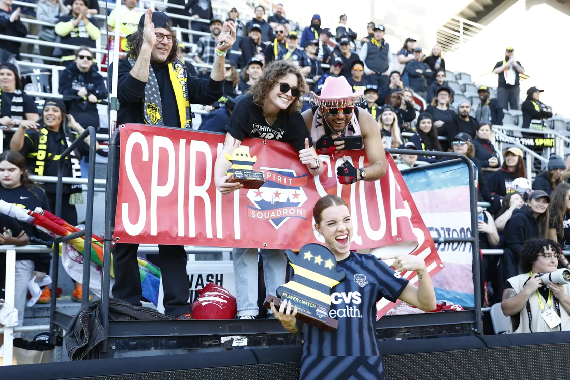 Hal Hershfelt holding up the GiGi in front of the Spirit Squadron banner on the capo in front of section 136
